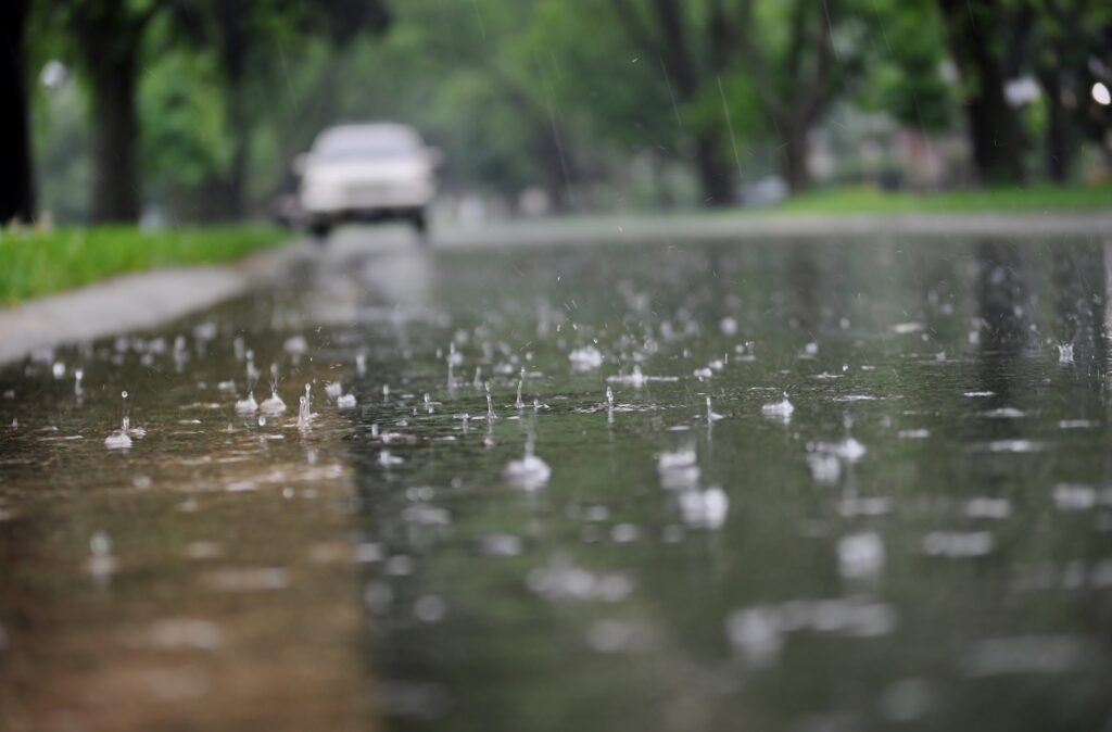 Wet road during a heavy storm, showing surface flooding and water pooling due to blocked or overwhelmed stormwater drainage systems.
